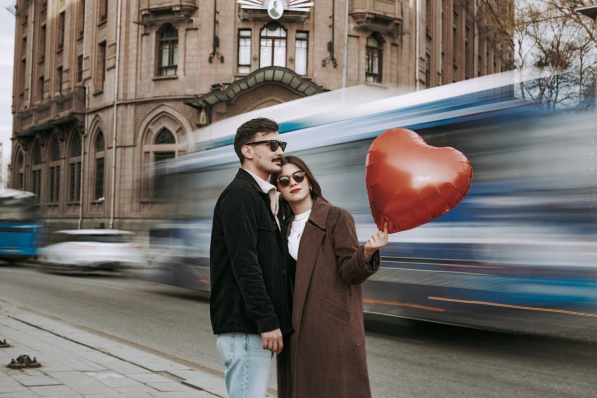 Romantic couple embracing with heart-shaped balloon in front of city street and blurred motion of vehicles.