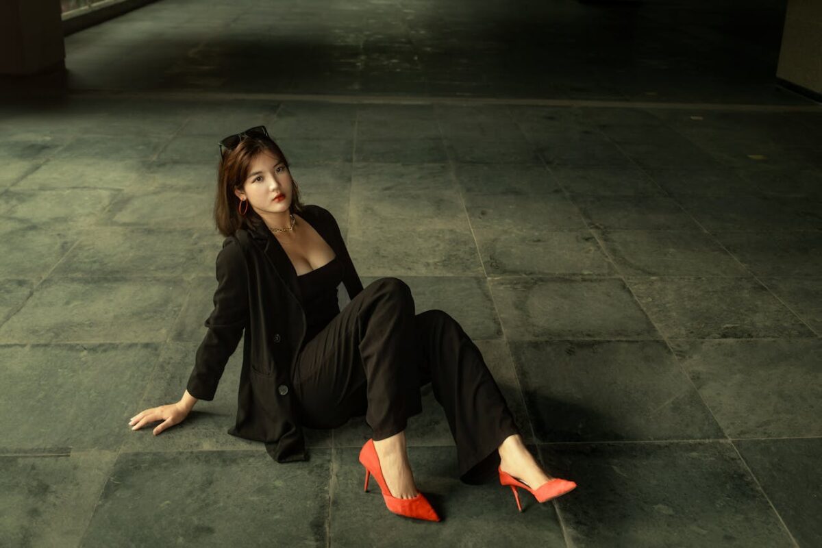 Elegant woman in black suit and red heels posing indoors, showcasing fashion style.