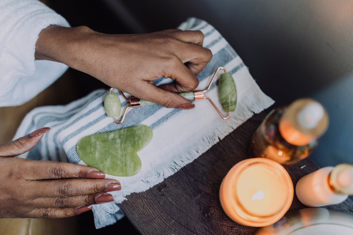 Overhead view of hands using a jade roller in a calming skincare routine with candles.