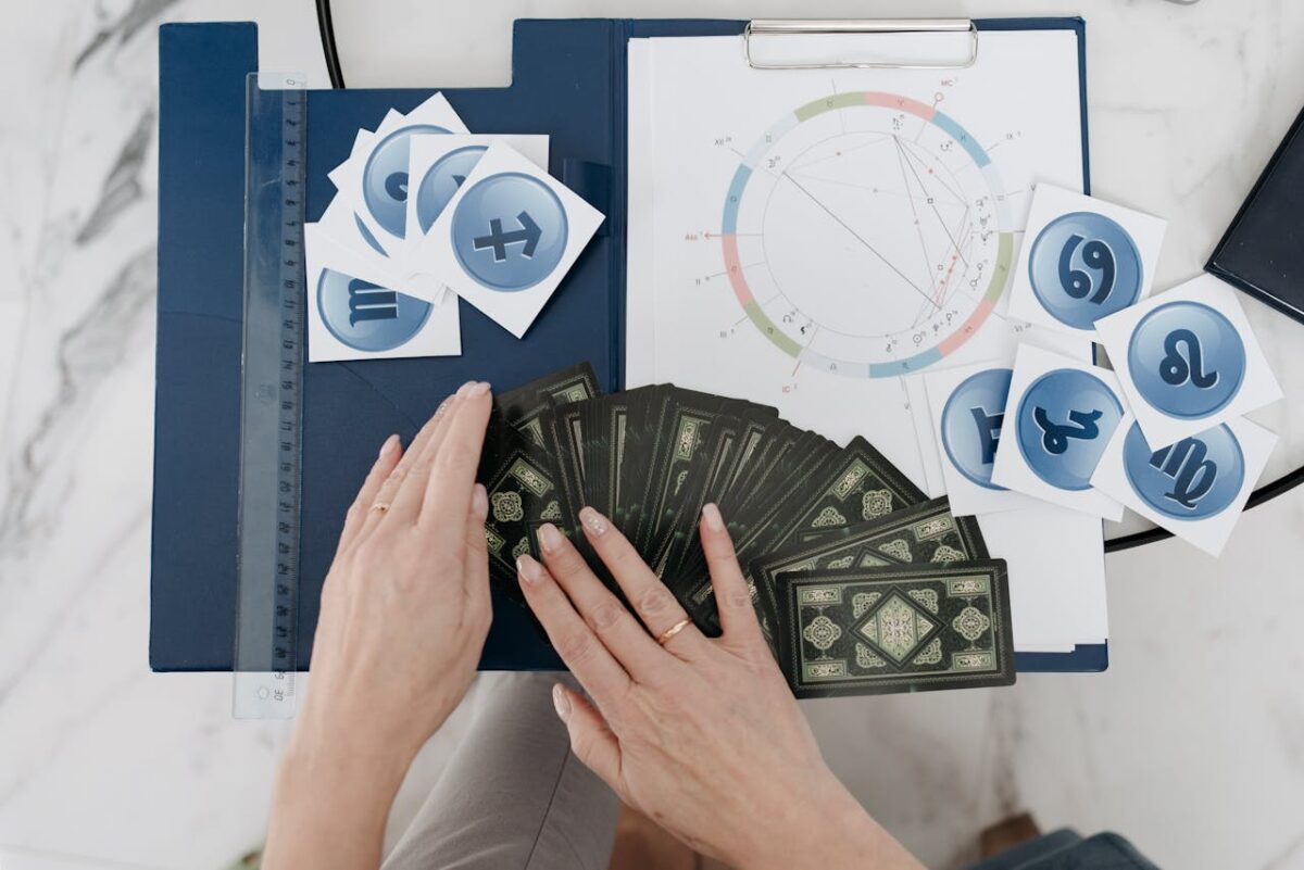 Hands arranging tarot cards with astrology symbols and natal chart on a table.